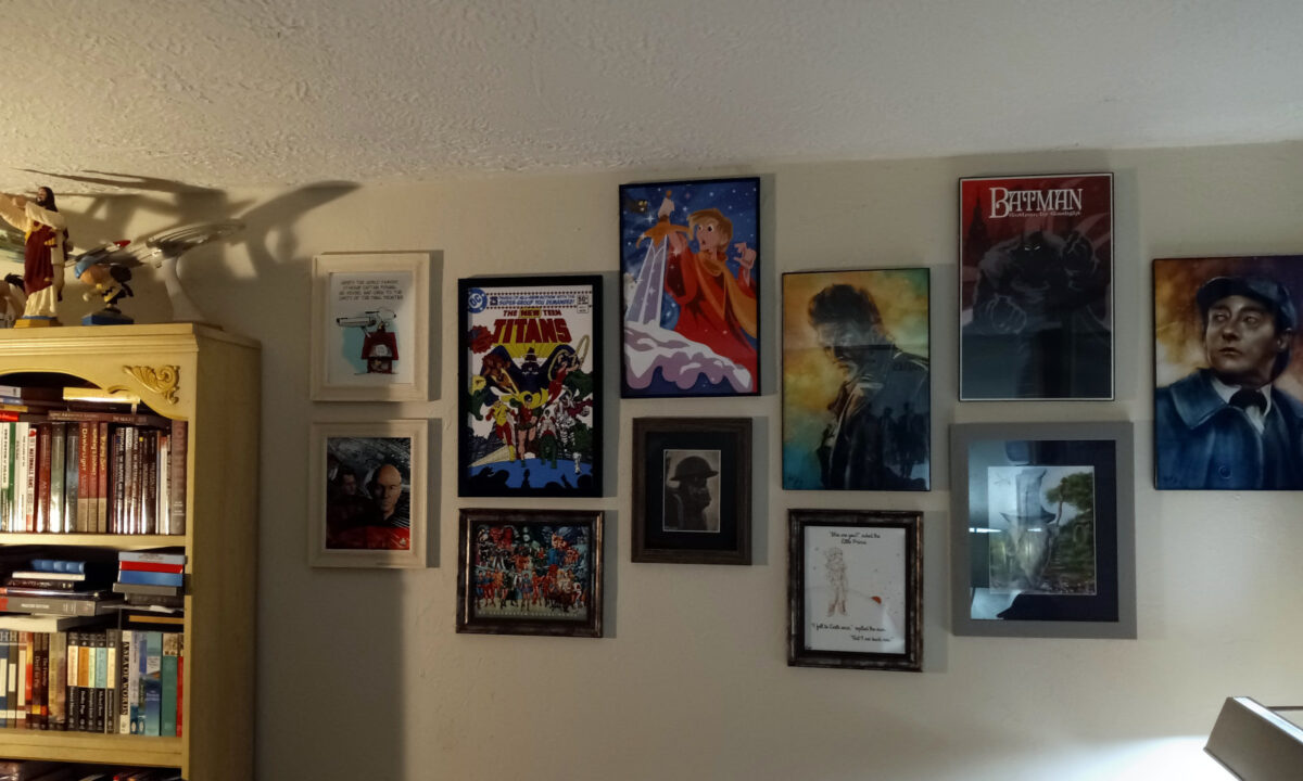 The gallery of fannish artwork on my bedroom wall, with the George Perez tribute piece hanging beneath a reproduction of the cover to New Teen Titans #1. Diamond Select Toys' Buddy Christ statue is at left.