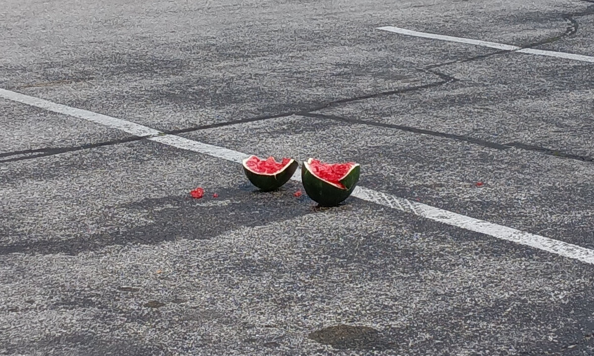 The two halves of a watermelon, dropped in a grocery store parking lot