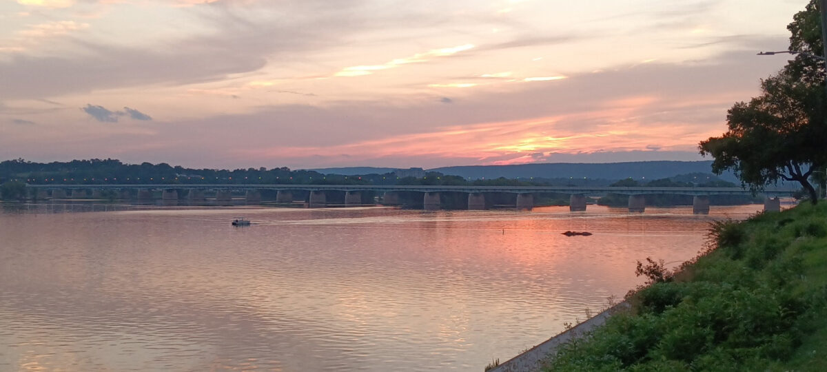 A pleasure boat passes beneath a bridge on the Susquehanna River, as seen from the river bank along Front Street