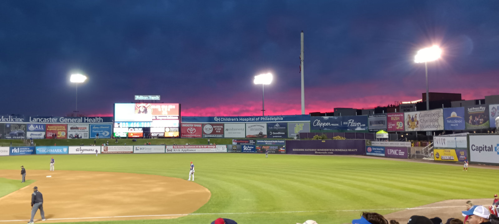 A pinkish, overcast sky in the west at sunset, beyond the outfield walls.