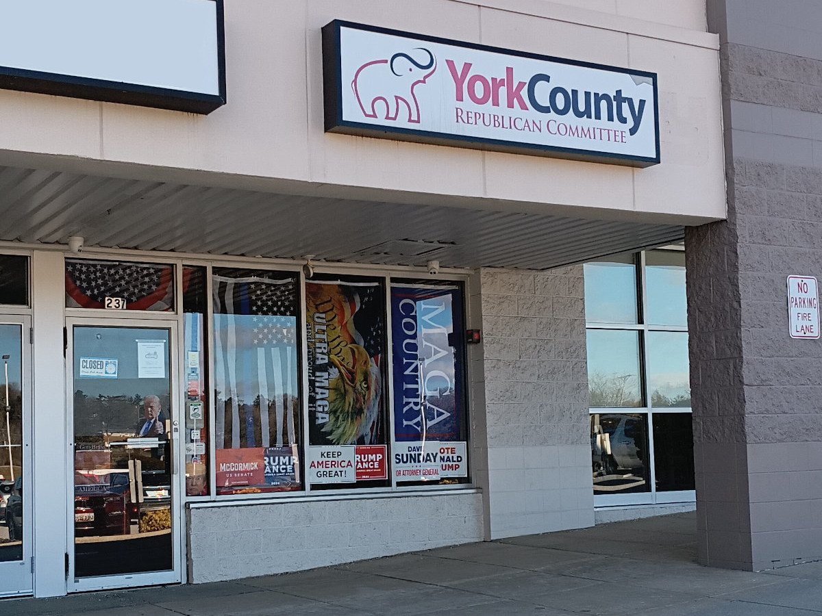 The York County GOP offices in the Giant shopping center, with a picture of Trump giving a thumbs-up on the door, plus a Thin Blue Line flag, an Ultra MAGA flag (with a bald eagle and the Constitution), and a MAGA Country flag across the windows.