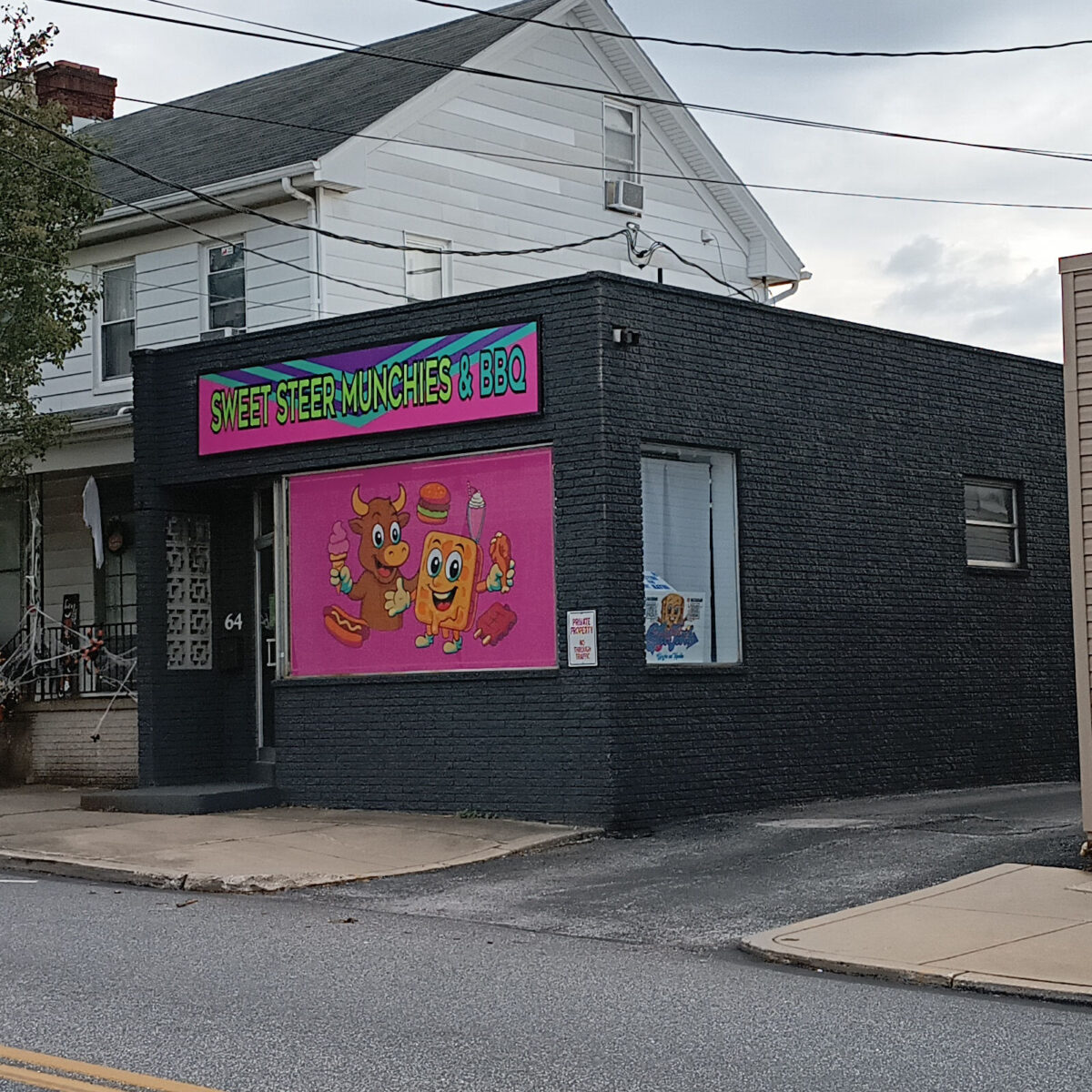 A business that's painted a dark gray and has a painting of a cartoon cow and a cartoon waffle holding ice cream cones and chicken wings.
