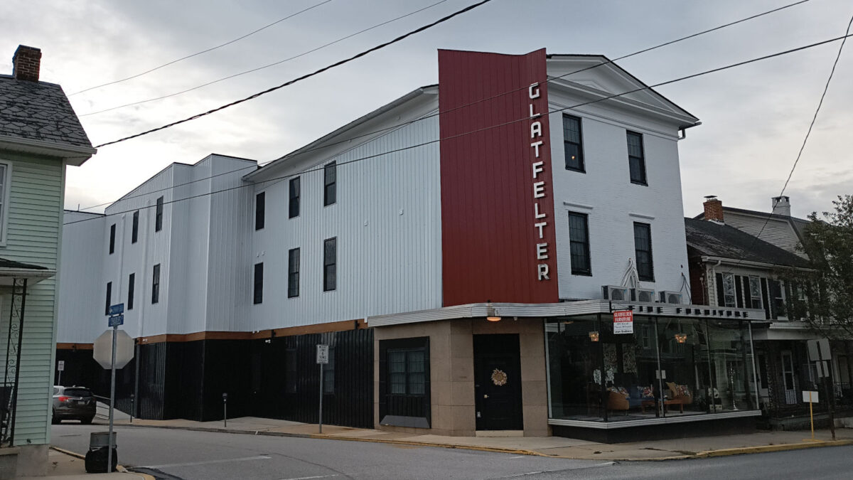 A building with a showcase window filled with furniture and a 1940s style sign that says "Glatfelter."
