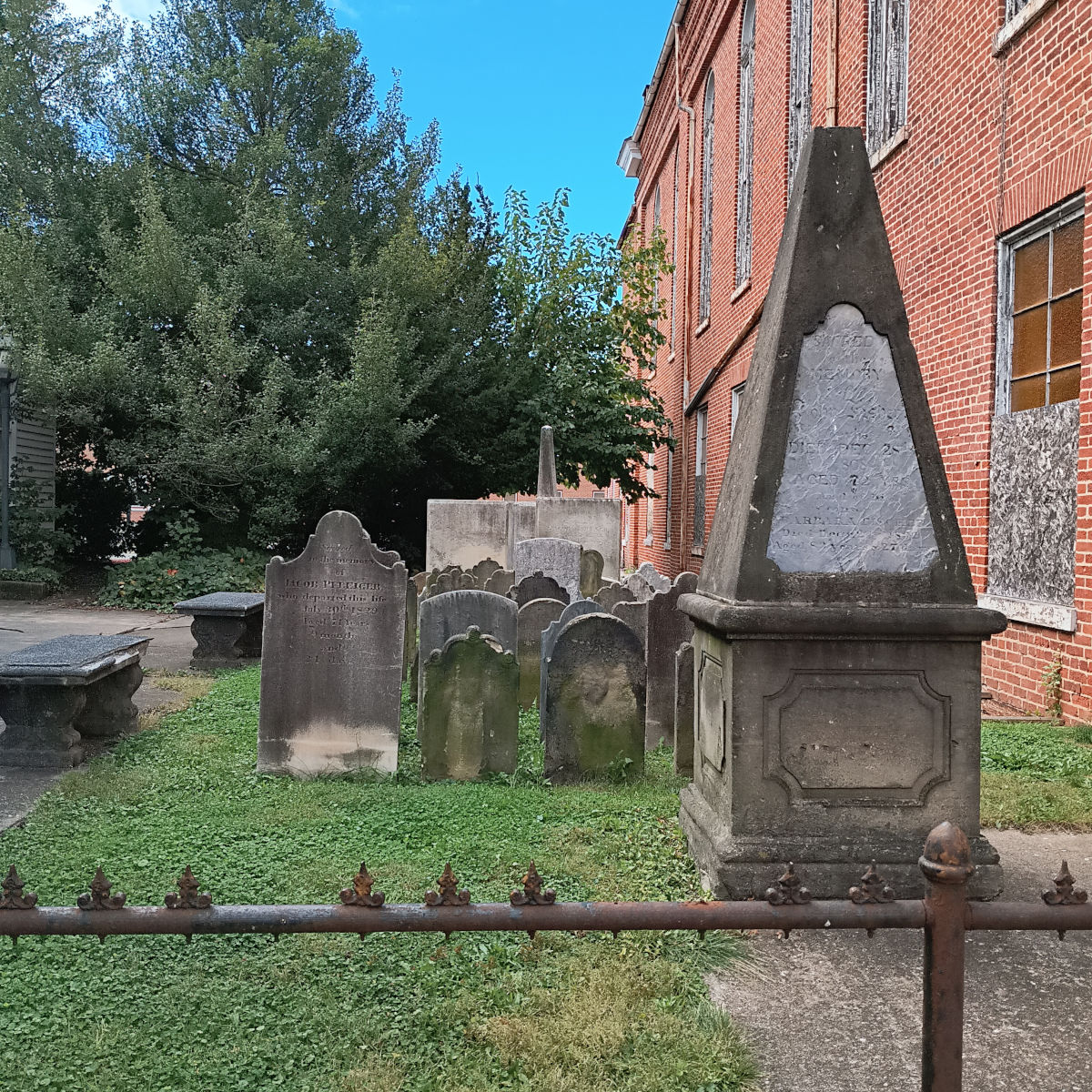 Photograph of the cemetery plot at the church. B large pyramidoid monument front, and old slab stones in several rows behind it. There's an obelisk at the far end.