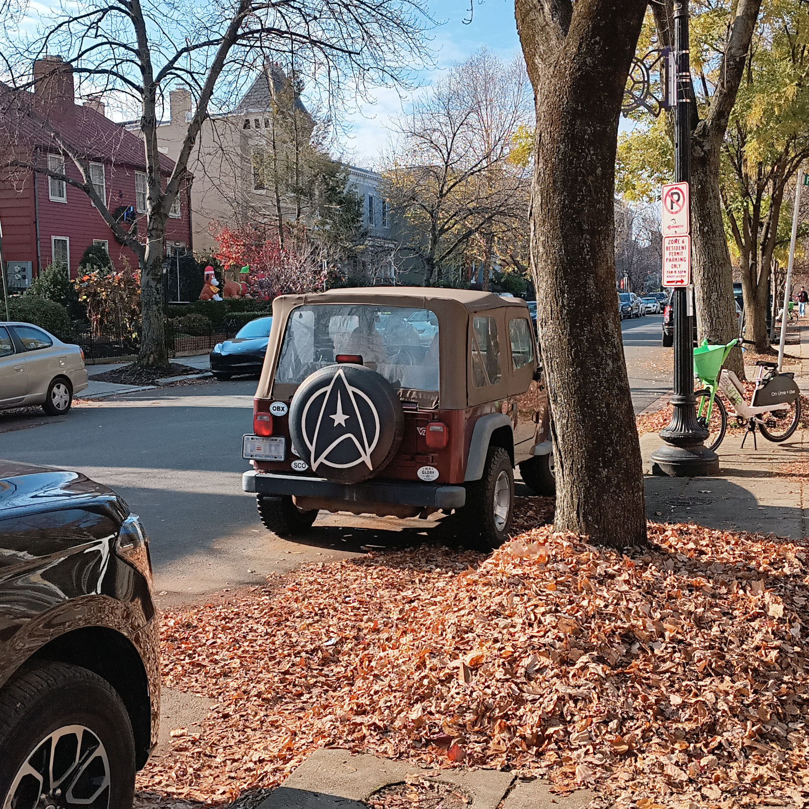 A Jeep, parked along a leaf-covered street, with a Star Trek Delta shield on its tire cover.