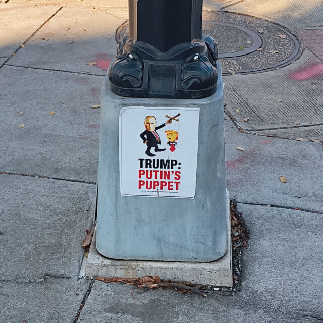 A sign on a lamppost that shows Donald Trump as a puppet, controlled by Vladimir Putin, with the caption: Trump Putin's Putin