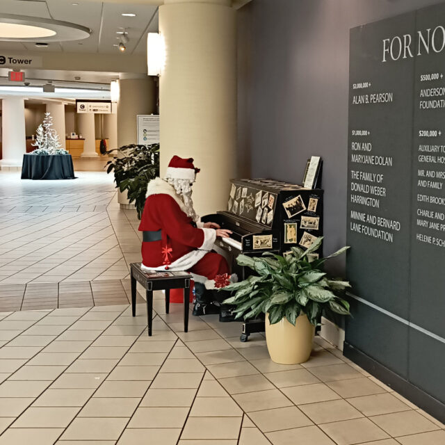 Santa Claus sitting at a piano in the lobby of Lynchburg General Hospital, playing Christmas songs