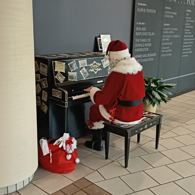 Santa Claus sitting at a piano in the lobby of Lynchburg General Hospital, playing Christmas songs