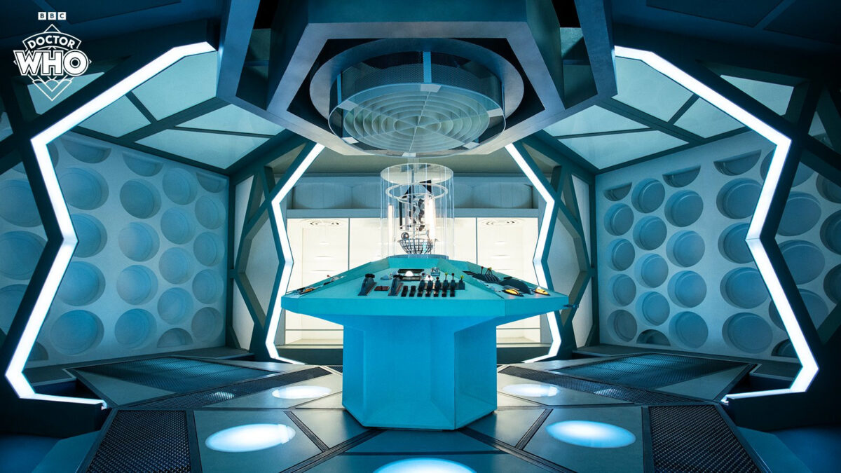 Official BBC image of the Fugitive Doctor's console room, with a light blue console, blueish walls, roundels, and an illuminated floor