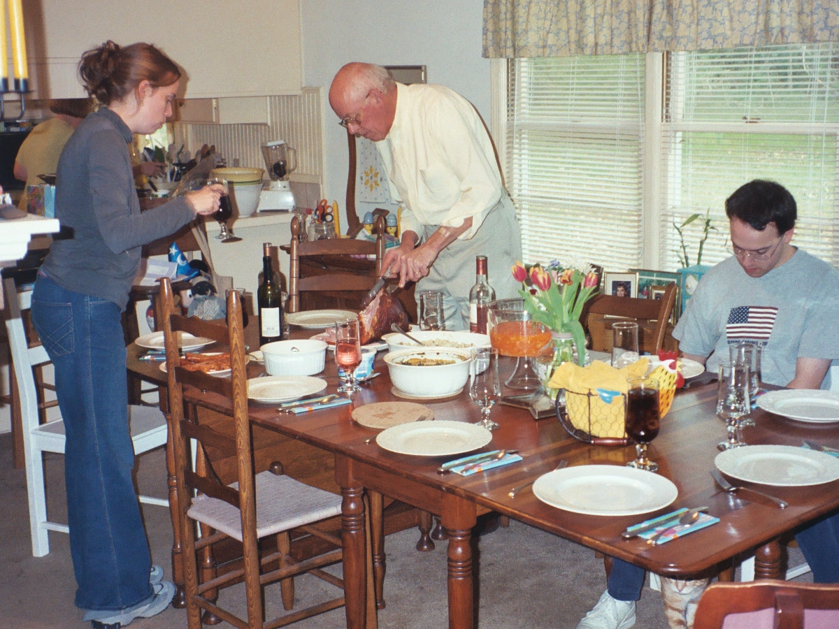 My dad, cutting the ham he cooked on the charcoal grill. My sister is pouring wine, my brother is reading something, and Leo, a cat, is under the table.